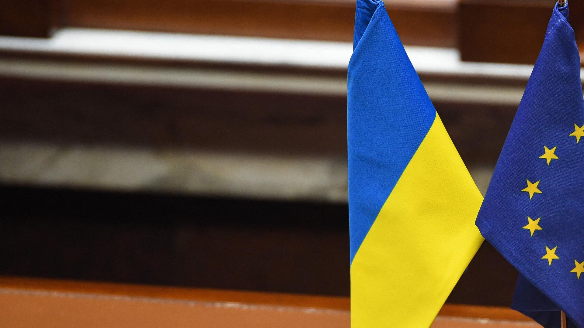 Flaggen der Ukraine und der EU stehen im Miniaturformat auf einem Schreibtisch