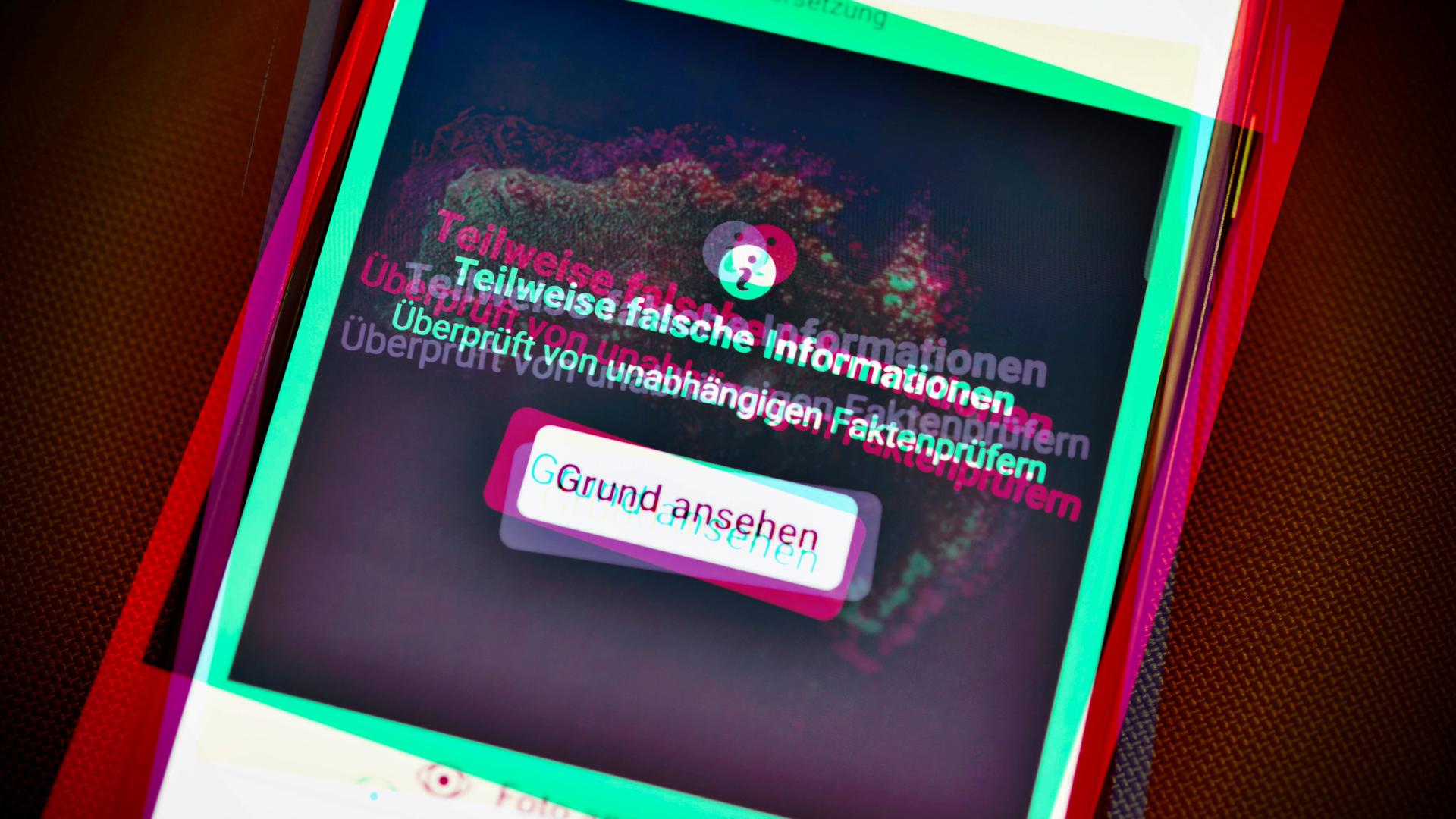 Ein Smartphone mit aufgedeckter Falschinformation in einem sozialen Netzwerk. Die Farbgebung ist an Tik Tok angelehnt.