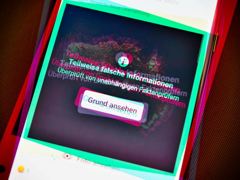 Ein Smartphone mit aufgedeckter Falschinformation in einem sozialen Netzwerk. Die Farbgebung ist an Tik Tok angelehnt.