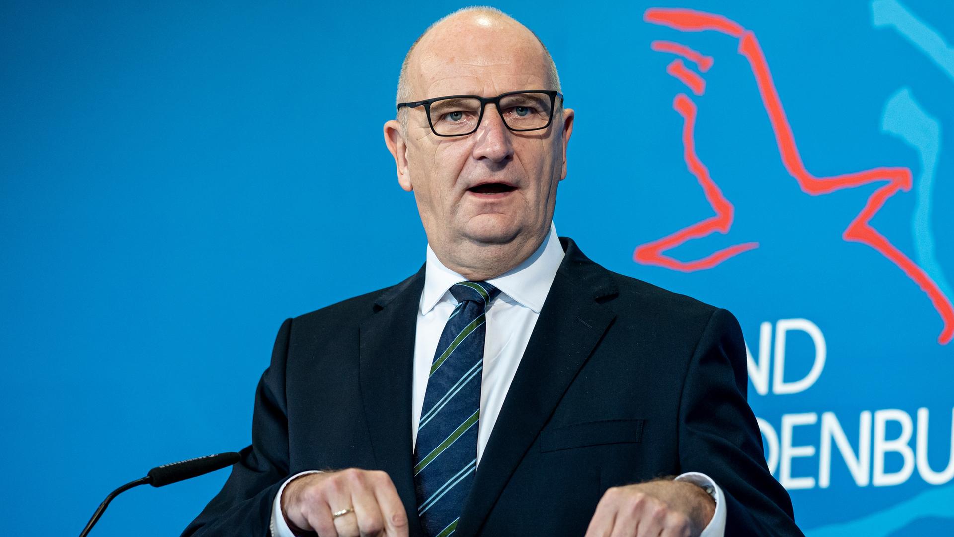 Dietmar Woidke (SPD), der Ministerpräsident von Brandenburg, spricht auf einer Pressekonferenz.  Hinter ihm ist eine blaue Rückwand mit Teilen des Schriftzugs "Brandenburg" und einem Vogelsymbol.