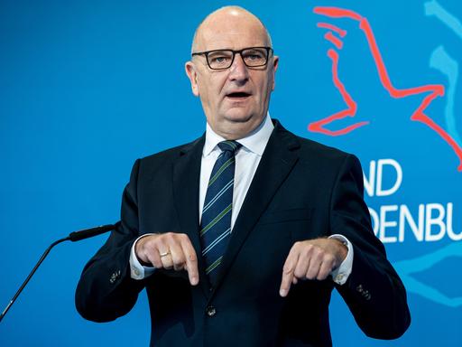 Dietmar Woidke (SPD), der Ministerpräsident von Brandenburg, spricht auf einer Pressekonferenz.  Hinter ihm ist eine blaue Rückwand mit Teilen des Schriftzugs "Brandenburg" und einem Vogelsymbol.