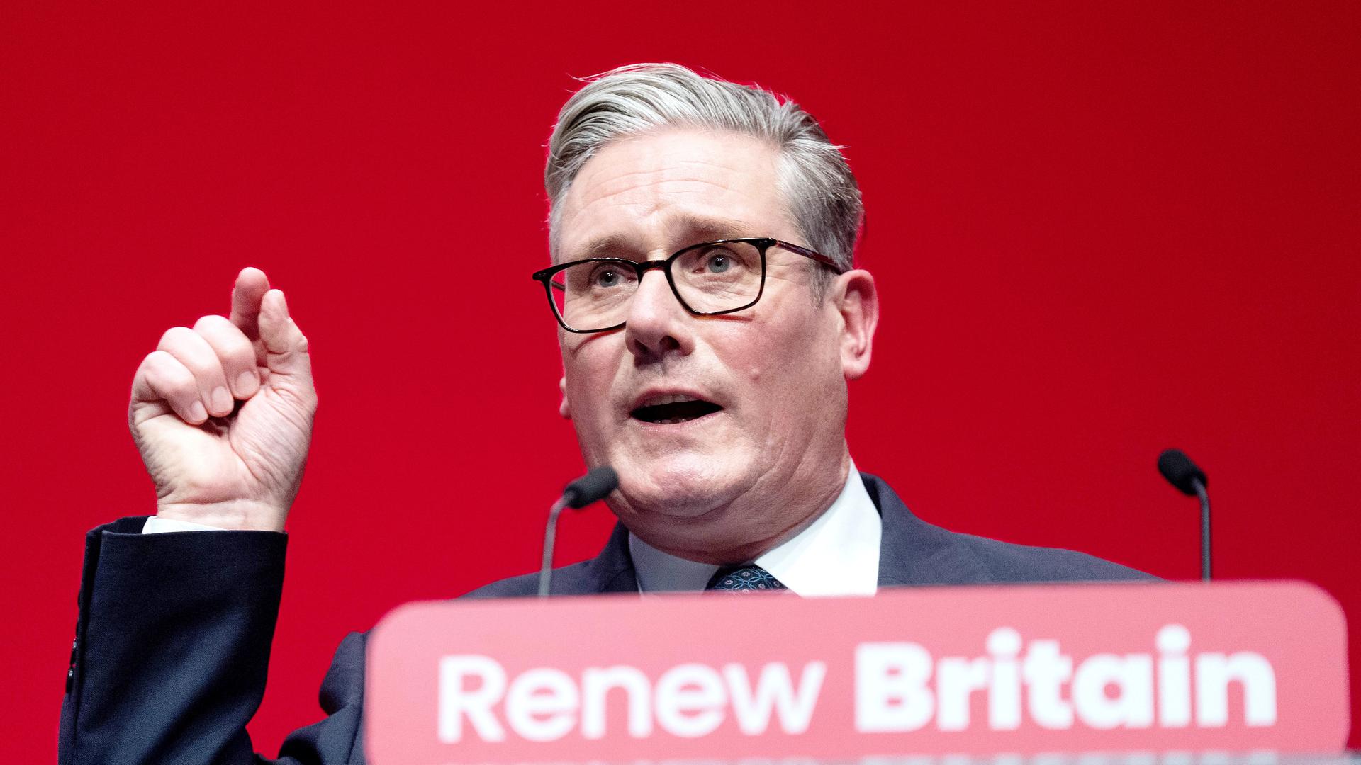 Keir Starmer hält eine Rede. Er hat die Hand gehoben und den Zeigefinger gestreckt. Er sieht entschlossen aus.
