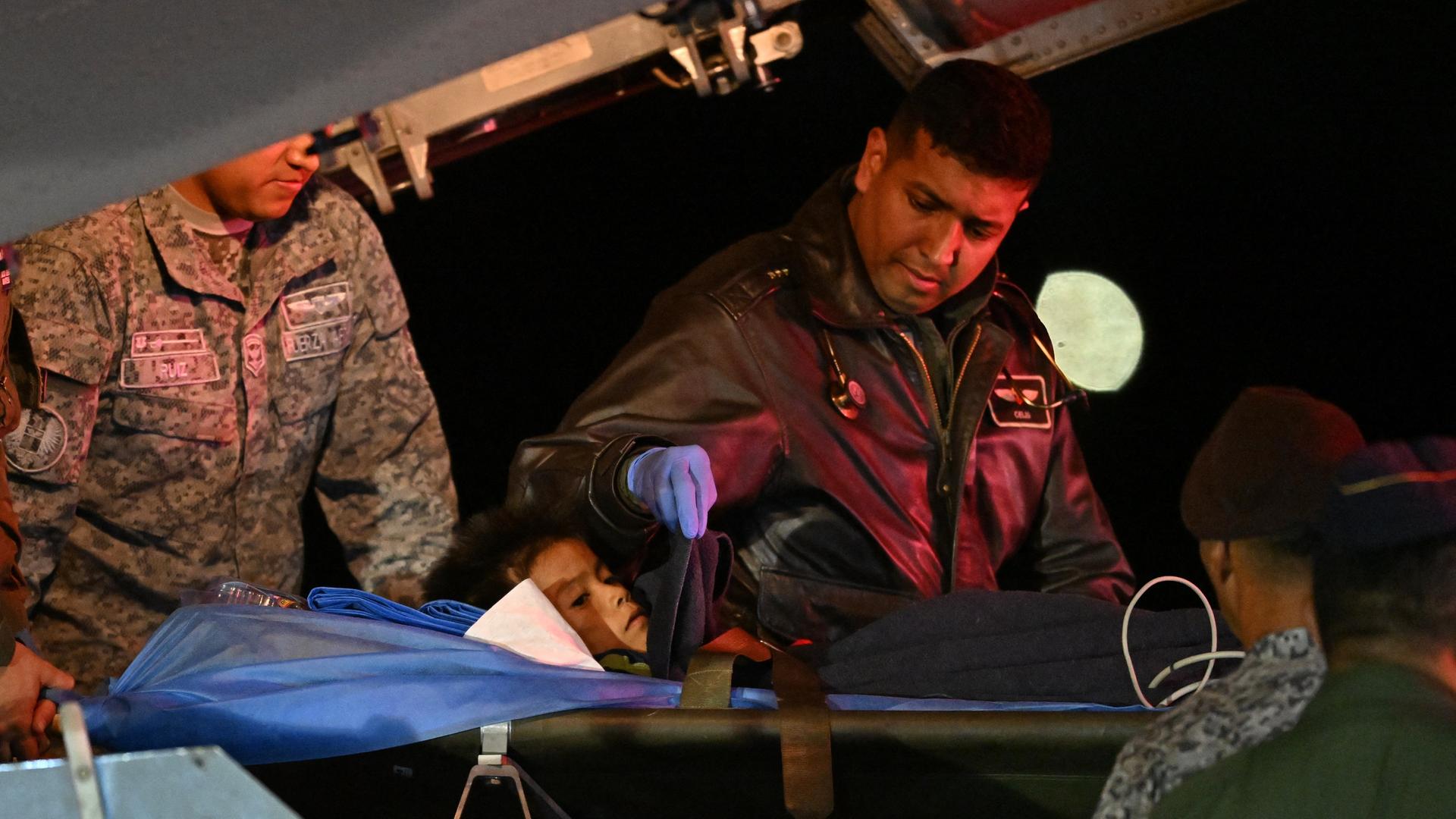 Ein Kind wird auf einer Trage aus einem Flugzeug geschoben, begleitet von Soldaten.