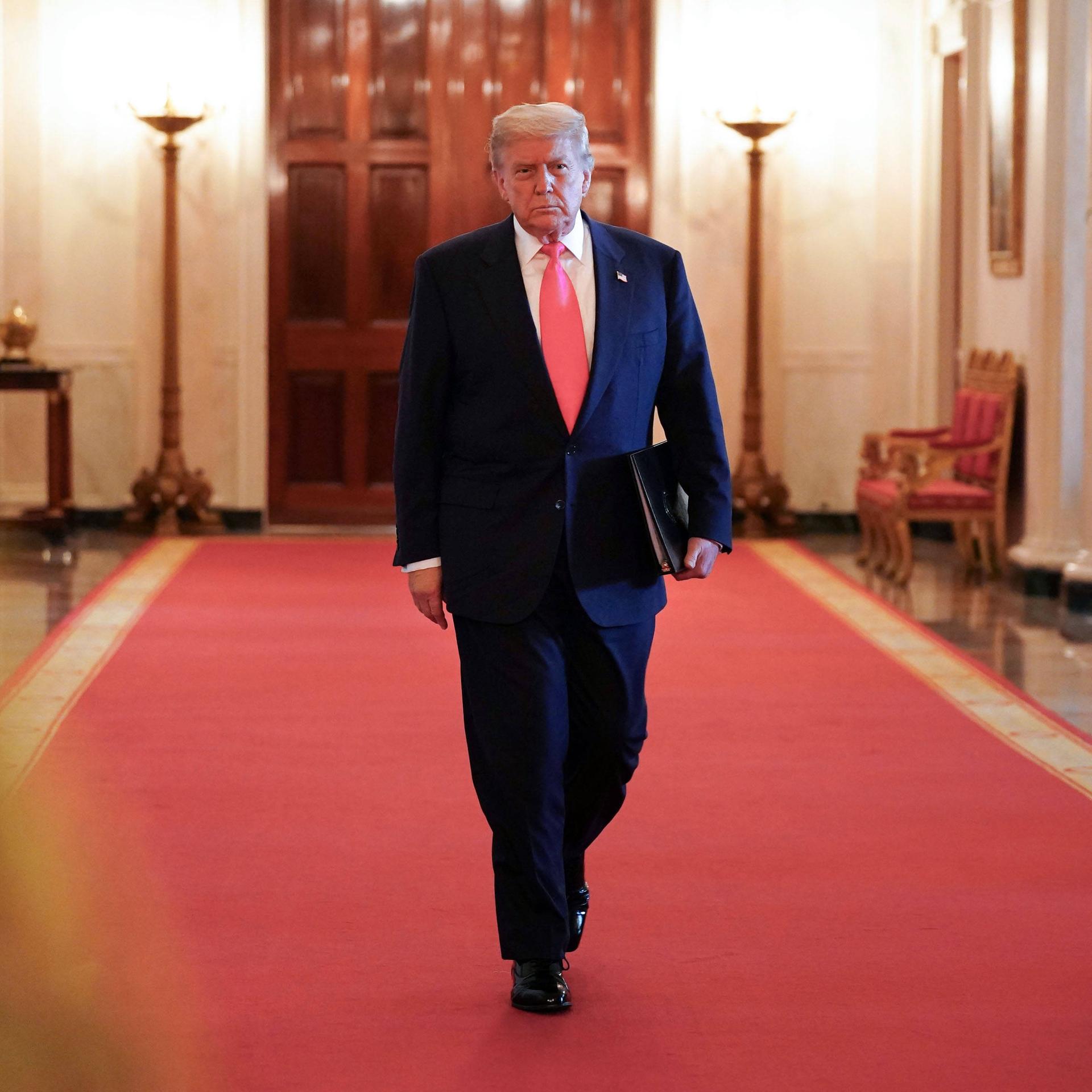 Donald Trump mit Aktenmappe unter dem Arm auf dem roten teppich in einem Korridor des Weißen Hauses Donald Trump mit Aktenmappe unter dem Arm auf dem roten teppich in einem Korridor des Weißen Hauses