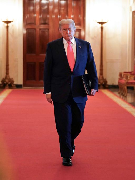 Donald Trump mit Aktenmappe unter dem Arm auf dem roten teppich in einem Korridor des Weißen Hauses