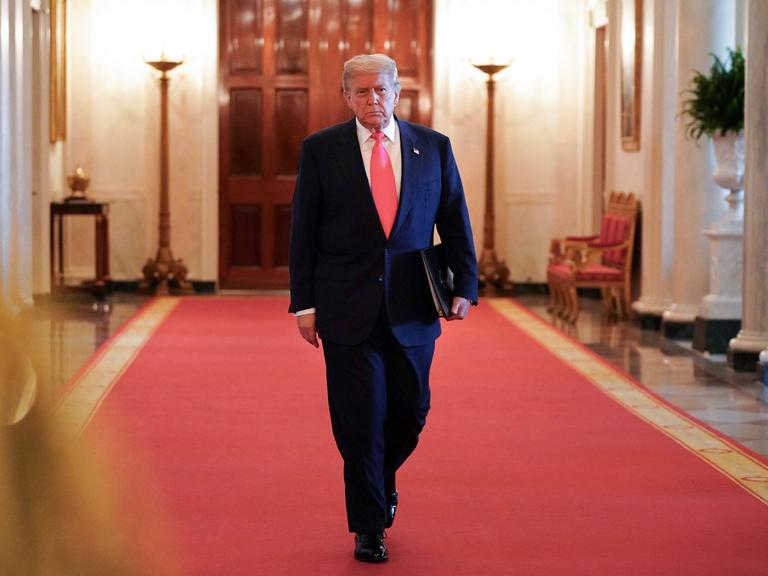 Donald Trump mit Aktenmappe unter dem Arm auf dem roten teppich in einem Korridor des Weißen Hauses