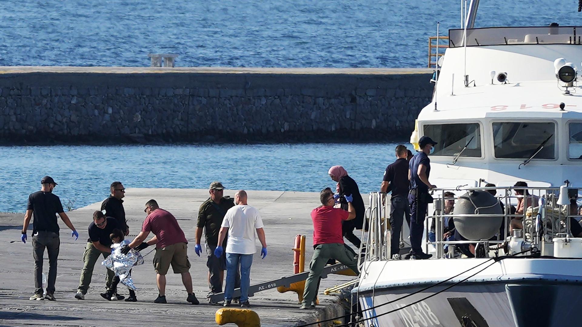 Griechenland, Lesbos: Ein Kind, das von Beamten der Küstenwache eskortiert wird, geht nach einer Rettungsaktion im Hafen von Mytilene mit anderen Migranten von Bord eines Schiffes. Griechenland, Lesbos: Ein Kind, das von Beamten der Küstenwache eskortiert wird, geht nach einer Rettungsaktion im Hafen von Mytilene mit anderen Migranten von Bord eines Schiffes.