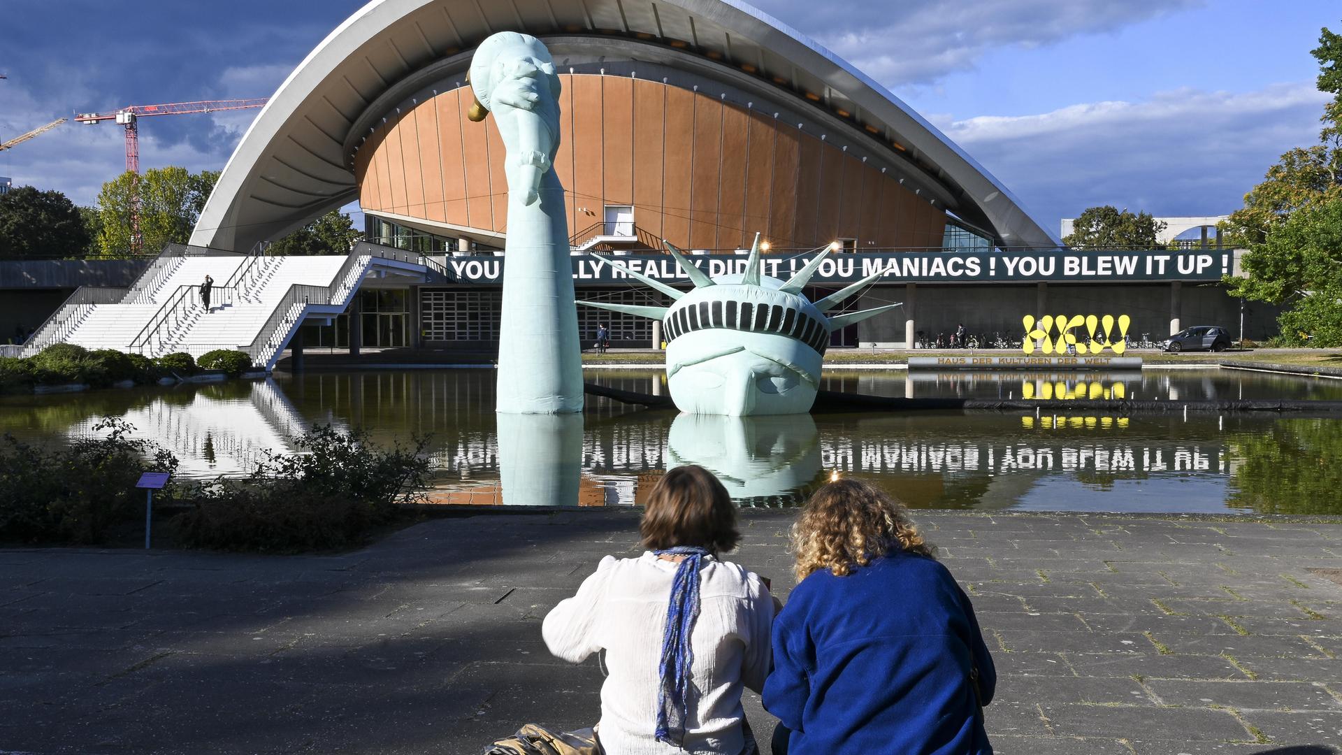 Im Rahmen der Ausstellung „Possibility of Unvernunft” in Berlin schauen zwei Besucherinnen auf eine aufblasbare Nachbildung der Freiheitsstatue, die im Brunnen vor dem Haus der Kulturen der Welt versunken ist.