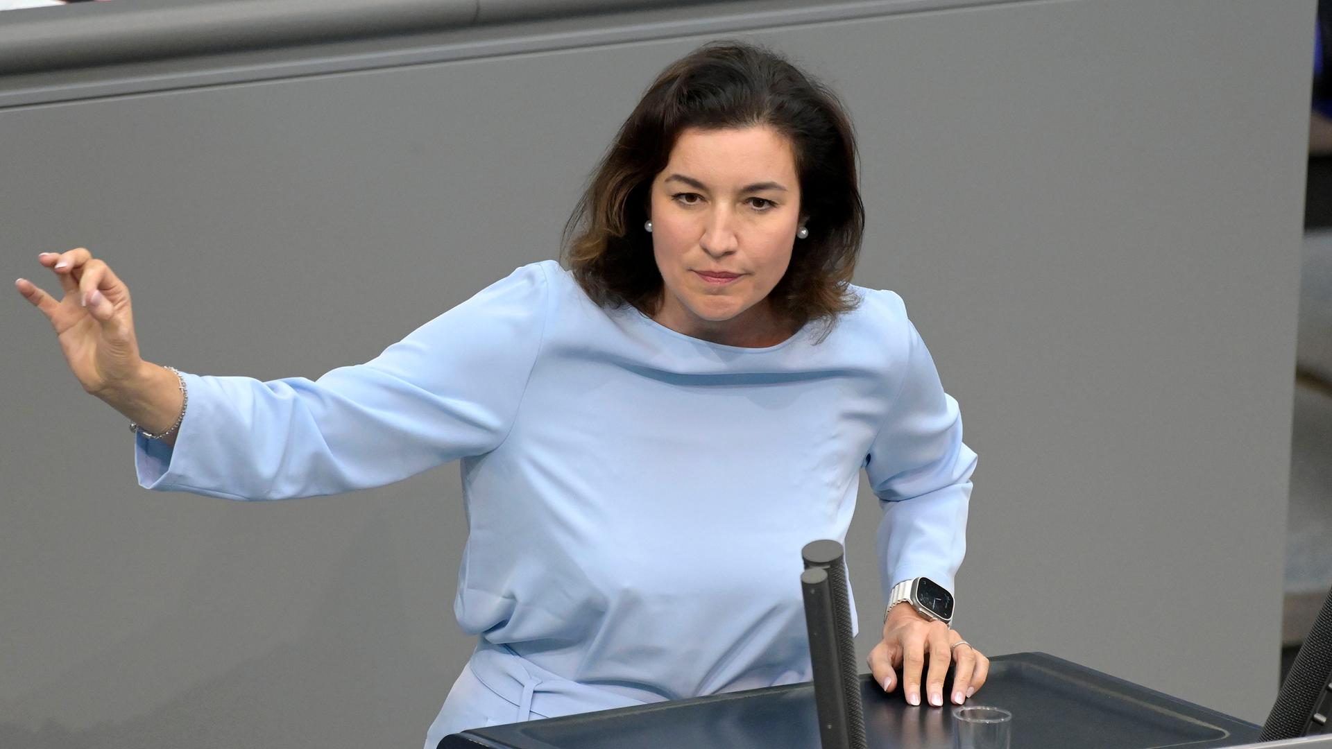 Dorothee Bär steht in einem hellblauen Einteiler hinter dem Rednerpult im Deutschen Bundestag und hebt einen Arm.