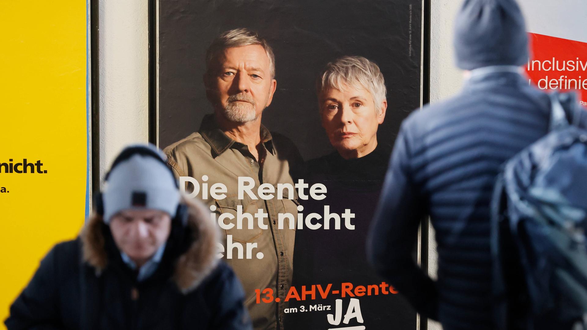 Ein "Ja"-Plakat zur 13. Monatsrente in der Schweiz. Abstimmung über eine 13. Monatsrente. Vor dem Plakat stehen ein Mann und eine ältere Frau. 23.02.2024
