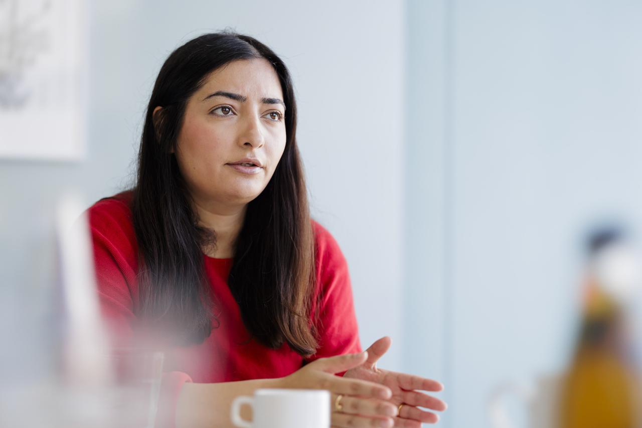 Reem Alabali-Radovan trägt ein rotes Oberteil, sitzt an einem Tisch und spricht gestikulierend.