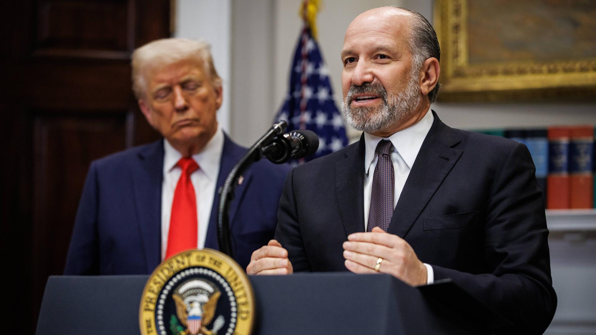 US-Handelsminister Lutnick spricht auf einer Pressekonferenz, im Hintergrund steht Präsident Trump.