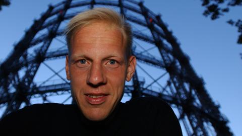 Der Filmemacher Jörg Buttgereit schaut in die Kamera, hinter ihm steht das ehemalige Gasometer in Berlin-Schöneberg.
