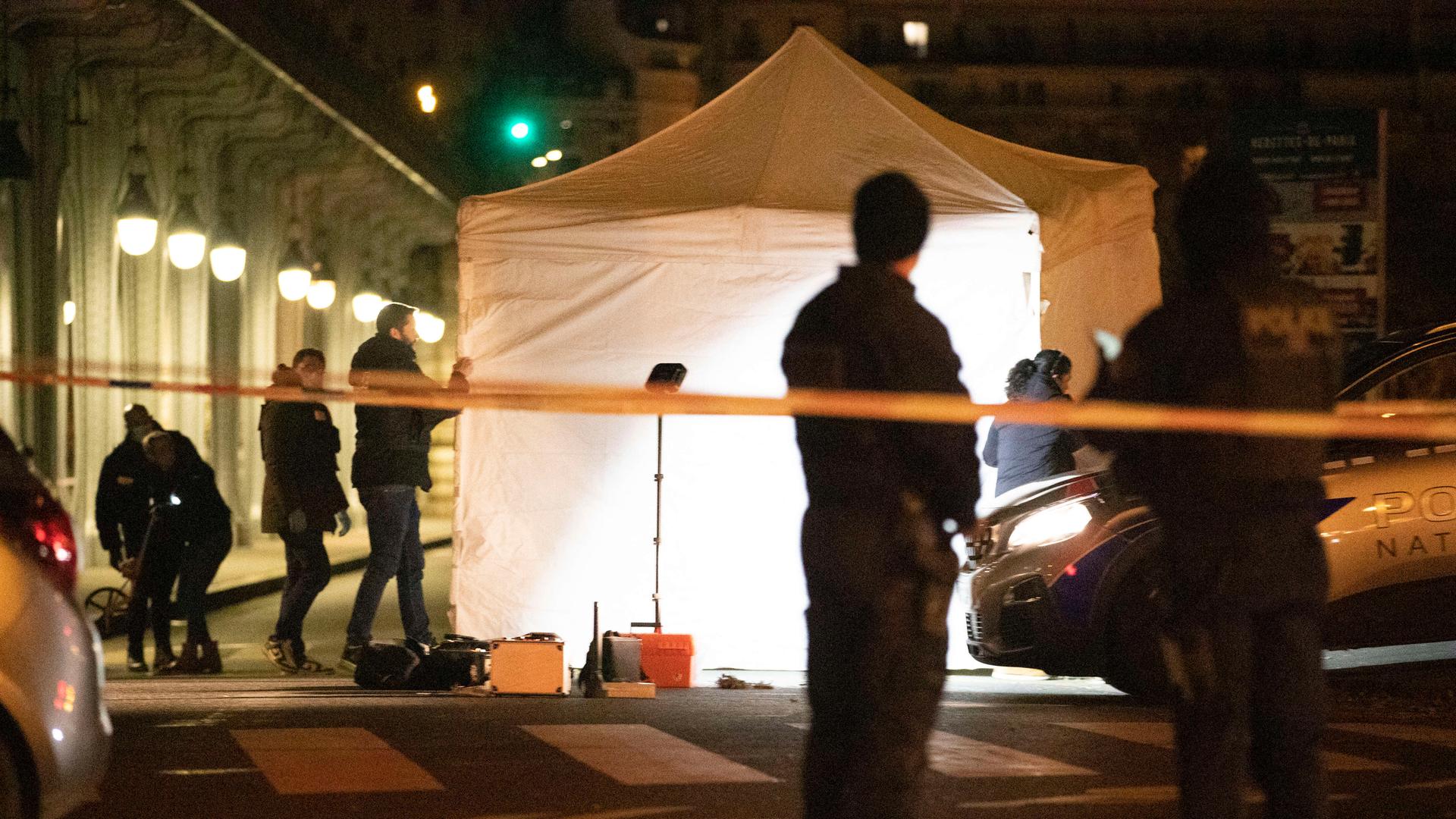 Blick auf ein aufgebautes weißes Zelt der Polizei, das beleuchtet ist. Darum herum sind in der Dunkelheit Mitarbeitende der französischen Kriminalpolizei zu sehen.