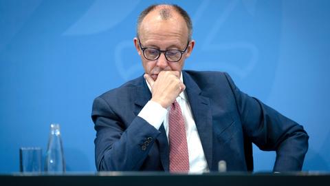 Bundeskanzler Friedrich Merz sitzt an einem Tisch; rechts neben ihm ein Glas Wasser; er stützt sich mit dem Kopf auf die rechte Hand.