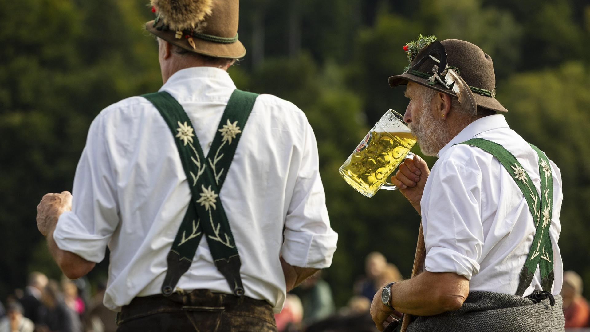 Zwei Männer in traditioneller Kleidung stehen beim Almabtrieb. Einer trinkt Bier aus einem großen Glas. Zwei Männer in traditioneller Kleidung stehen beim Almabtrieb. Einer trinkt Bier aus einem großen Glas.