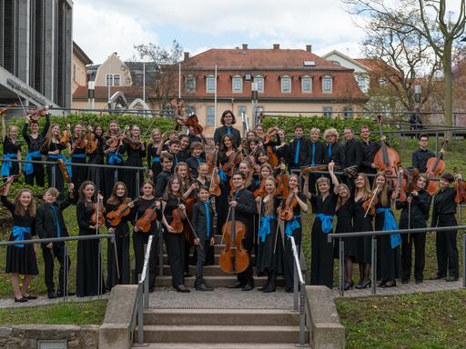 Die jungen Musikerinnen und Musiker der Deutschen Streicherphilharmonie stehen in Konzertkleidung mit ihren Instrumenten auf einer Freilufttreppe.