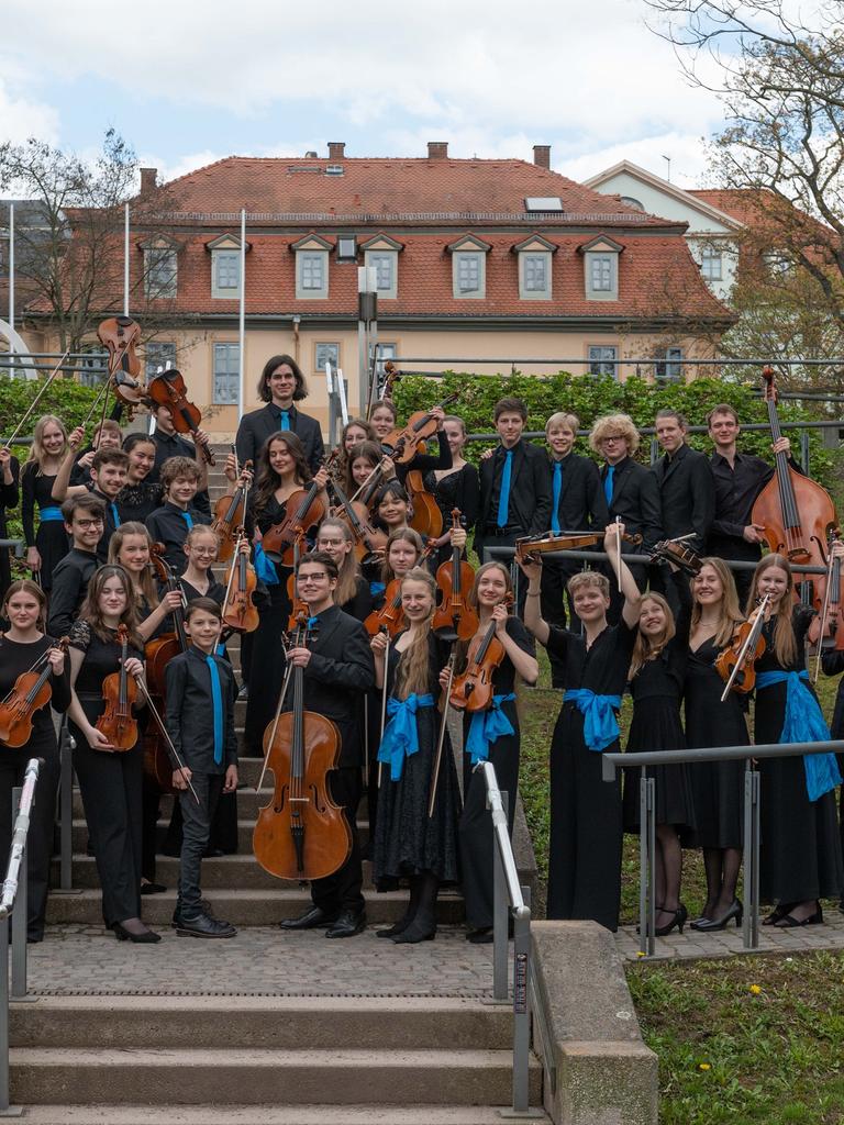 Die jungen Musikerinnen und Musiker der Deutschen Streicherphilharmonie stehen in Konzertkleidung mit ihren Instrumenten auf einer Freilufttreppe.