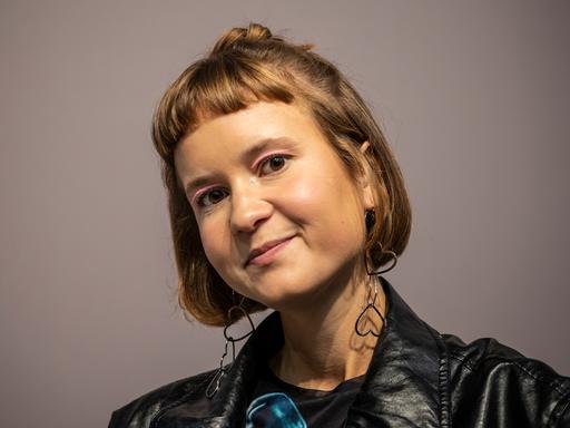 Caroline Wahl trägt eine schwarze Lederjacke, rosa Lidschatten und Ohrringe in Herzform. Sie schaut freundlich in die Kamera. Caroline Wahl trägt eine schwarze Lederjacke, rosa Lidschatten und Ohrringe in Herzform. Sie schaut freundlich in die Kamera.