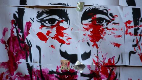 Rote Farbkleckse und Handabdrücke auf einer Zeichnung des Gesichts von Wladimir Putin.