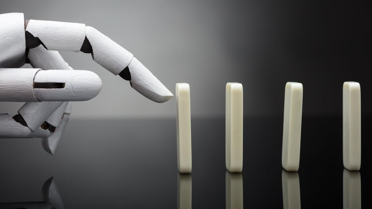 Eine Roboterhand ist kurz davor, einen aufgestellten Dominostein anzutippen.