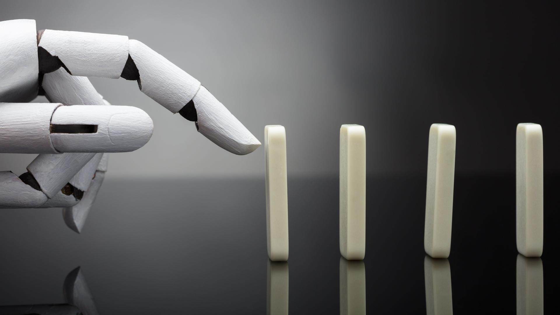 Eine Roboterhand ist kurz davor, einen aufgestellten Dominostein anzutippen.