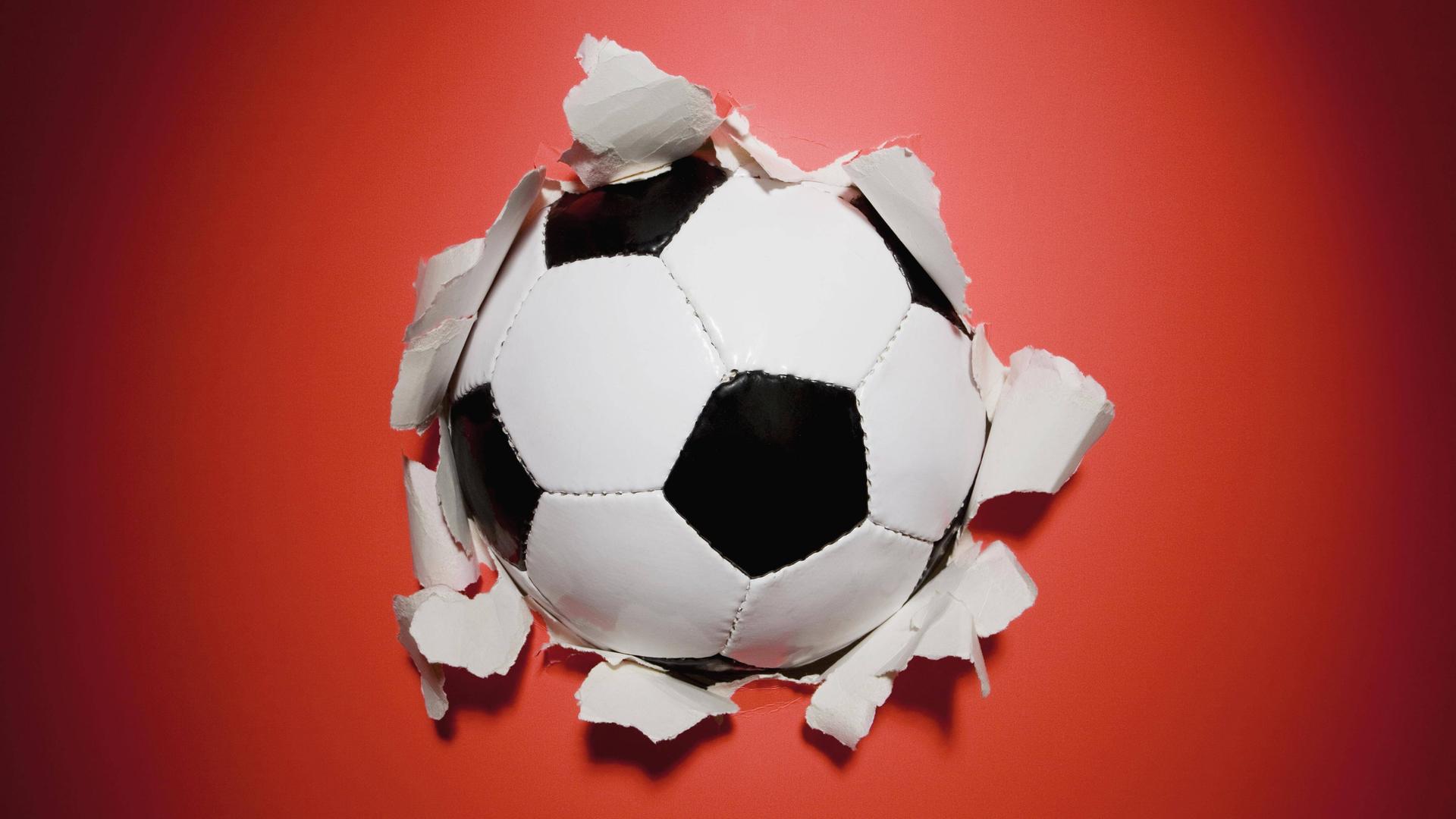 Ein schwarz-weißer Fußball durchbricht eine rote Wand.