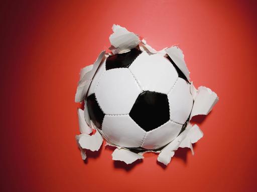 Ein schwarz-weißer Fußball durchbricht eine rote Wand.