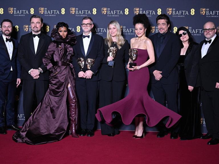 Beteiligte des Films "One Battle After Another" stehen nebeneinander auf dem Roten Teppich und präsentieren Preise.