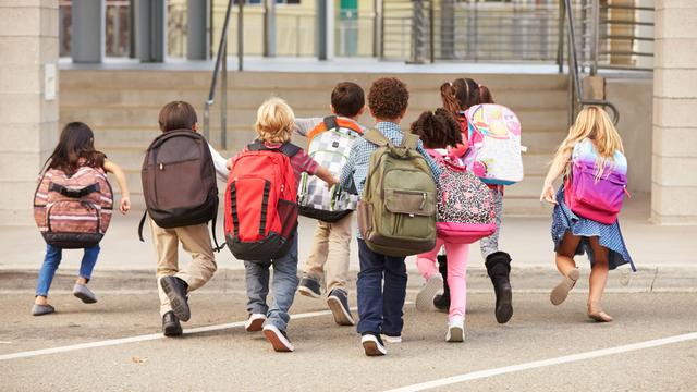 Kinder mit bunten Rucksäcken laufen auf einem Schul-Hof.