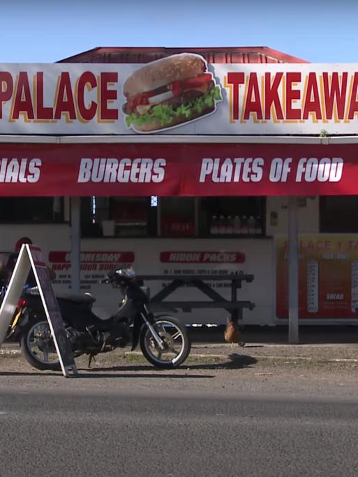 Eine Imbissbude mit rotem Dach und Burgerwerbung an einer Straße