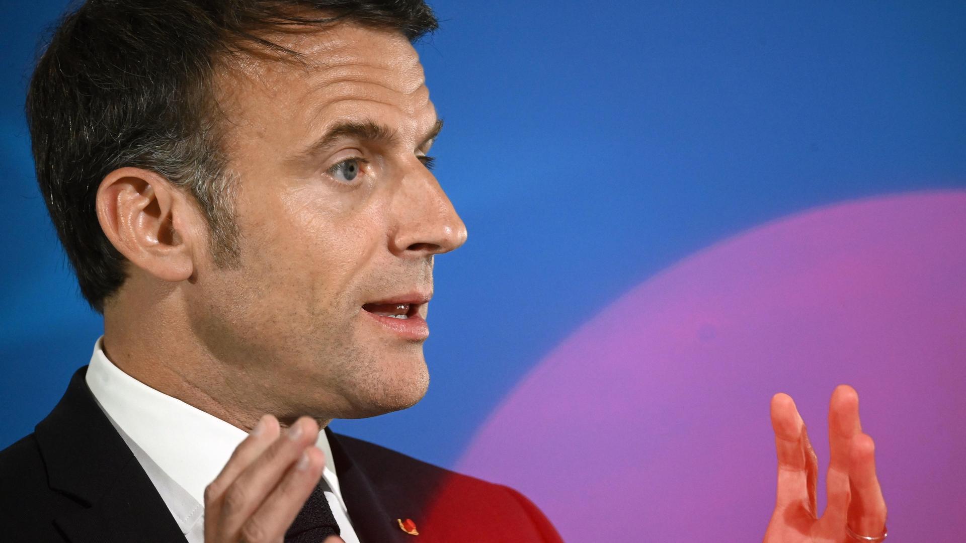Emmanuel Macron redet vor blauem Hintergrund und gestikuliert dabei.