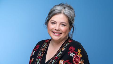 Die Köchin Maria Groß, mit schwarzem mit Blumen gemusterten Kleid vor blauem Hintergrund, aufgenommen am Rande der MDR Talkshow "Riverboat" am 18.03.2022 in Leipzig.