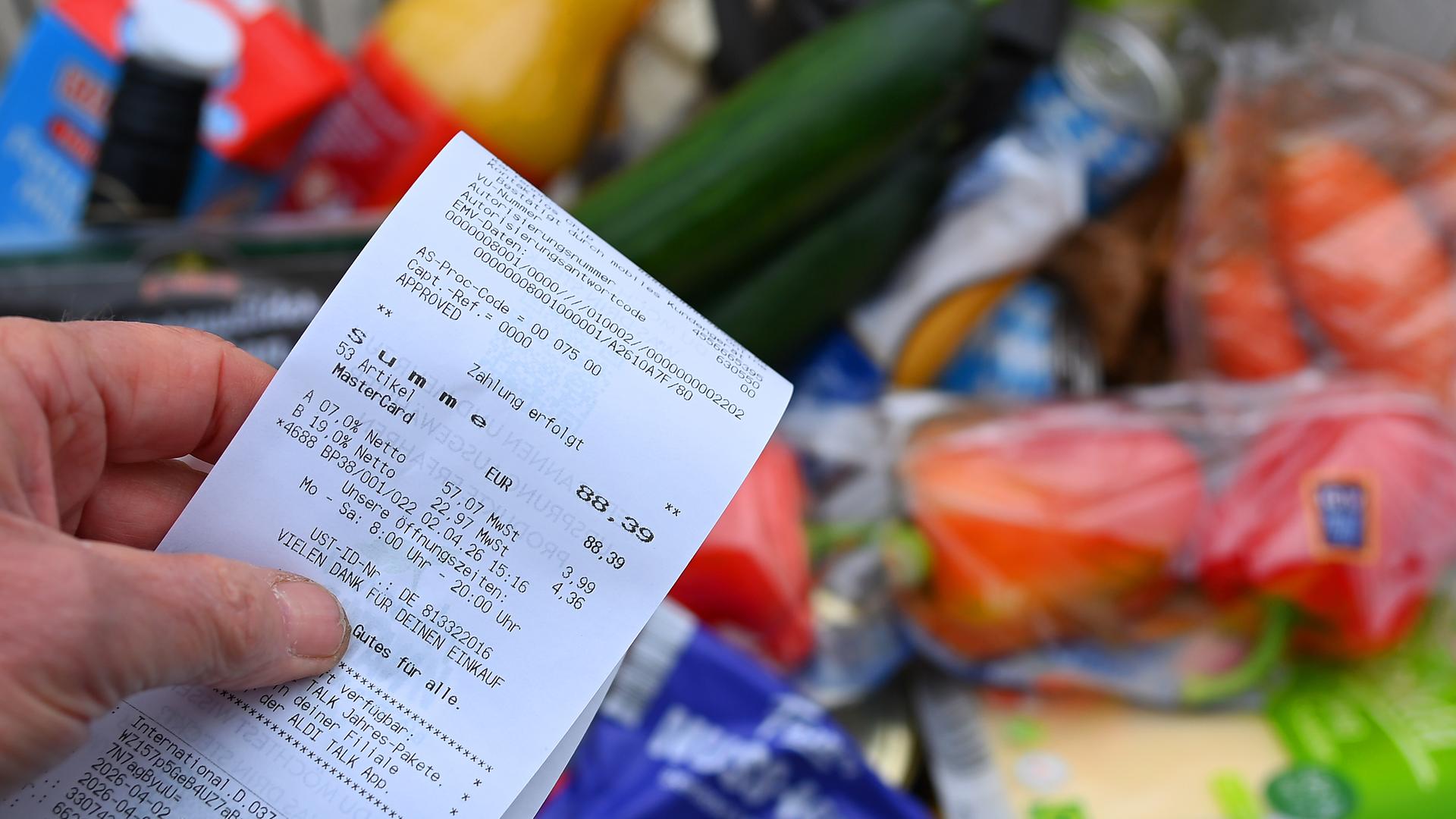 Eine Hand hält einen Einkaufszettel über einem Lebensmittel-Einkauf