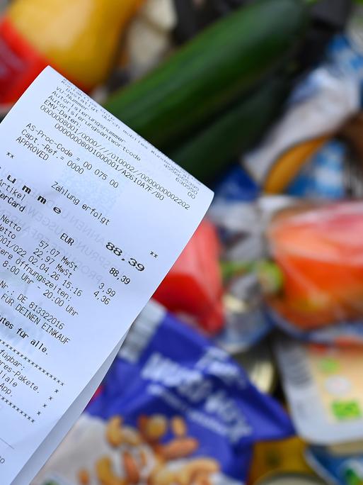 Eine Hand hält einen Einkaufszettel über einem Lebensmittel-Einkauf