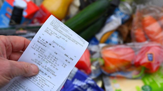 Eine Hand hält einen Einkaufszettel über einem Lebensmittel-Einkauf