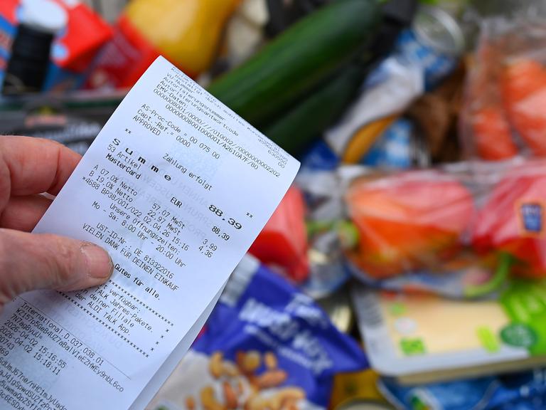 Eine Hand hält einen Einkaufszettel über einem Lebensmittel-Einkauf