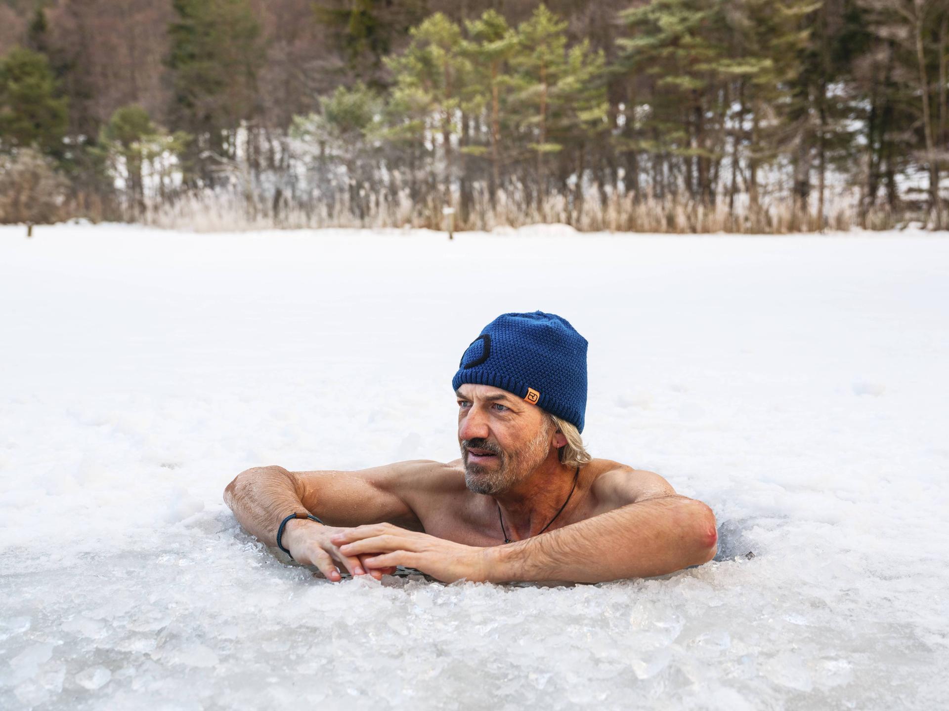 Ein Mann mit Mütze legt beim Eisbaden im Thumsee bei Bad Reichenhall in Bayern seine Arme auf die Eisoberfläche.