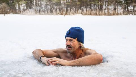 Ein Mann mit Mütze legt beim Eisbaden in einem Eisloch im Thumsee bei Bad Reichenhall in Bayern seine Arme auf die Eisoberfläch