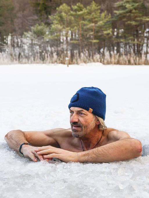 Ein Mann mit Mütze legt beim Eisbaden im Thumsee bei Bad Reichenhall in Bayern seine Arme auf die Eisoberfläche.