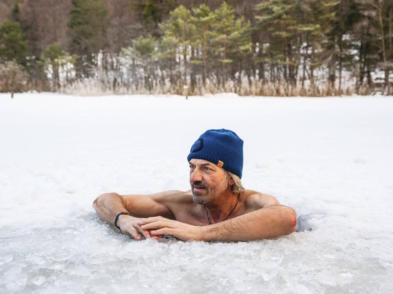 Ein Mann mit Mütze legt beim Eisbaden im Thumsee bei Bad Reichenhall in Bayern seine Arme auf die Eisoberfläche.