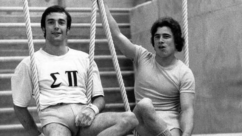 Eberhard Gienger (links, BRD) und Wolfgang Thüne (rechts, DDR) nebeneinander auf einem Turngerät, beide lächeln.