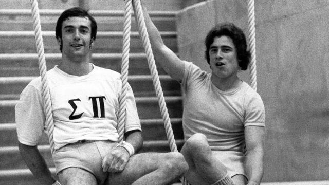 Eberhard Gienger (links, BRD) und Wolfgang Thüne (rechts, DDR) nebeneinander auf einem Turngerät, beide lächeln.