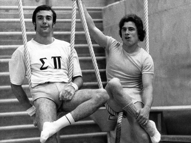 Eberhard Gienger (links, BRD) und Wolfgang Thüne (rechts, DDR) nebeneinander auf einem Turngerät, beide lächeln.