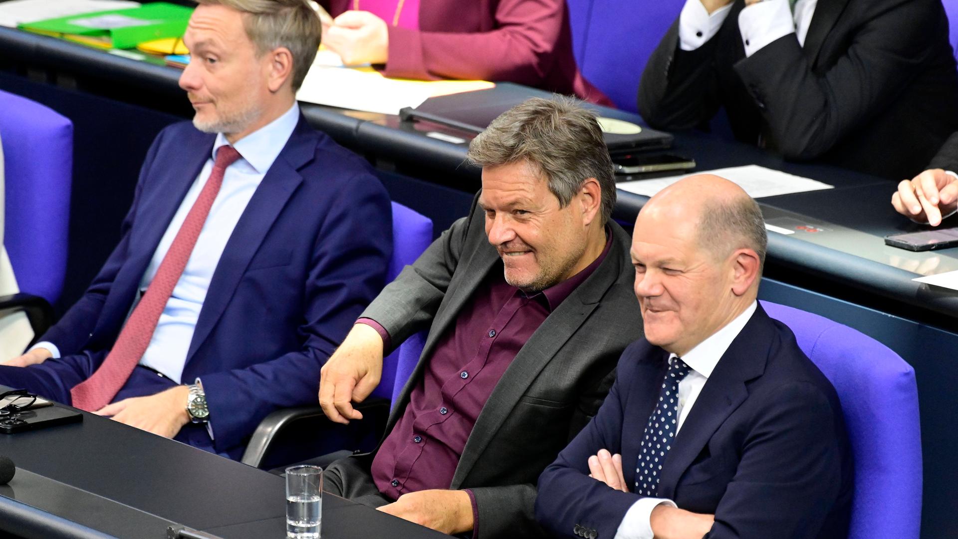 Christian Lindner, Robert Habeck und Olaf Scholz sitzen im Bundestag nebeneinander und grinsen