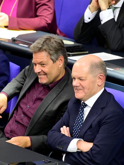 Christian Lindner, Robert Habeck und Olaf Scholz sitzen im Bundestag nebeneinander und grinsen