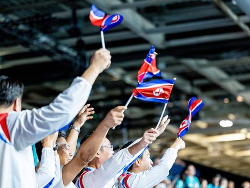 Nordkoreanische Fans winken Fahnen bei den Olympischen Spielen in Paris im Tischtennis.  