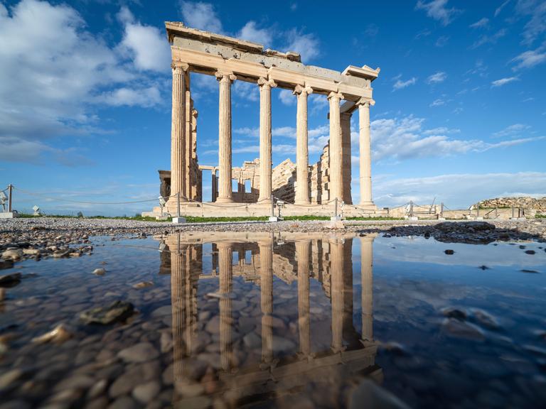 Auf dem Bild ist der Erechtheion Tempel auf der Athener Akropolis zu sehen, ein eindrucksvolles Gebäude aus großen Säulen, die ein Dach tragen.