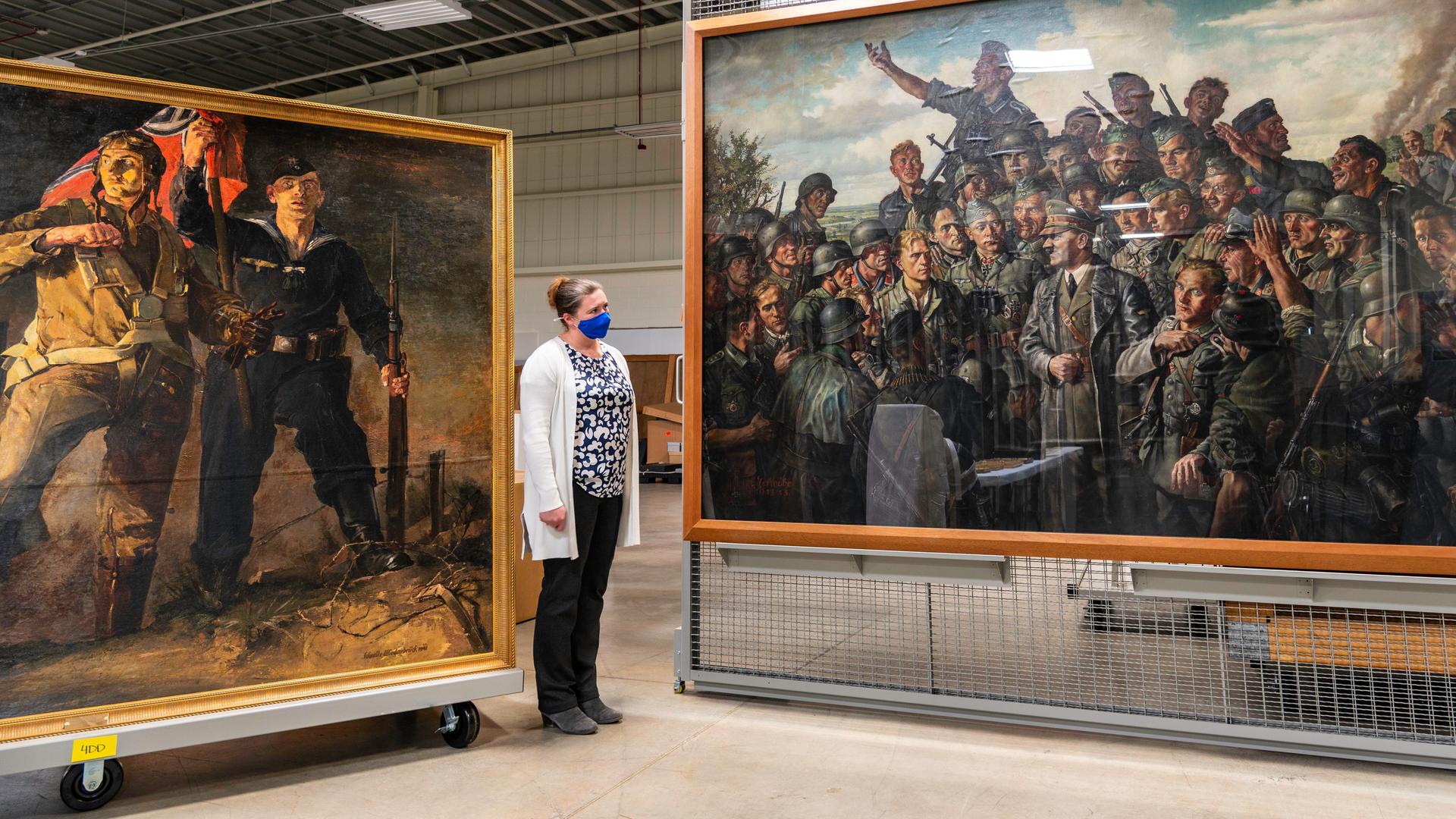 Eine Frau in einem weißen Kittel steht in einer großen Halle, wo Kunstwerke stehen. 