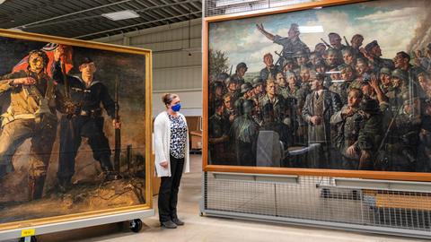 Eine Frau in einem weißen Kittel steht in einer großen Halle, wo Kunstwerke stehen. 